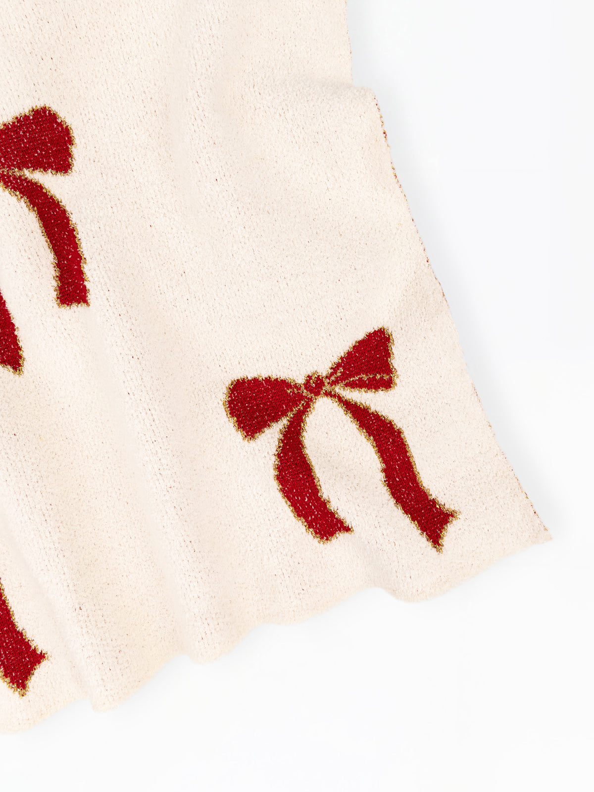 Close-up of a cream-colored knit fabric with red glittery bow patterns, shown against a plain white background.
