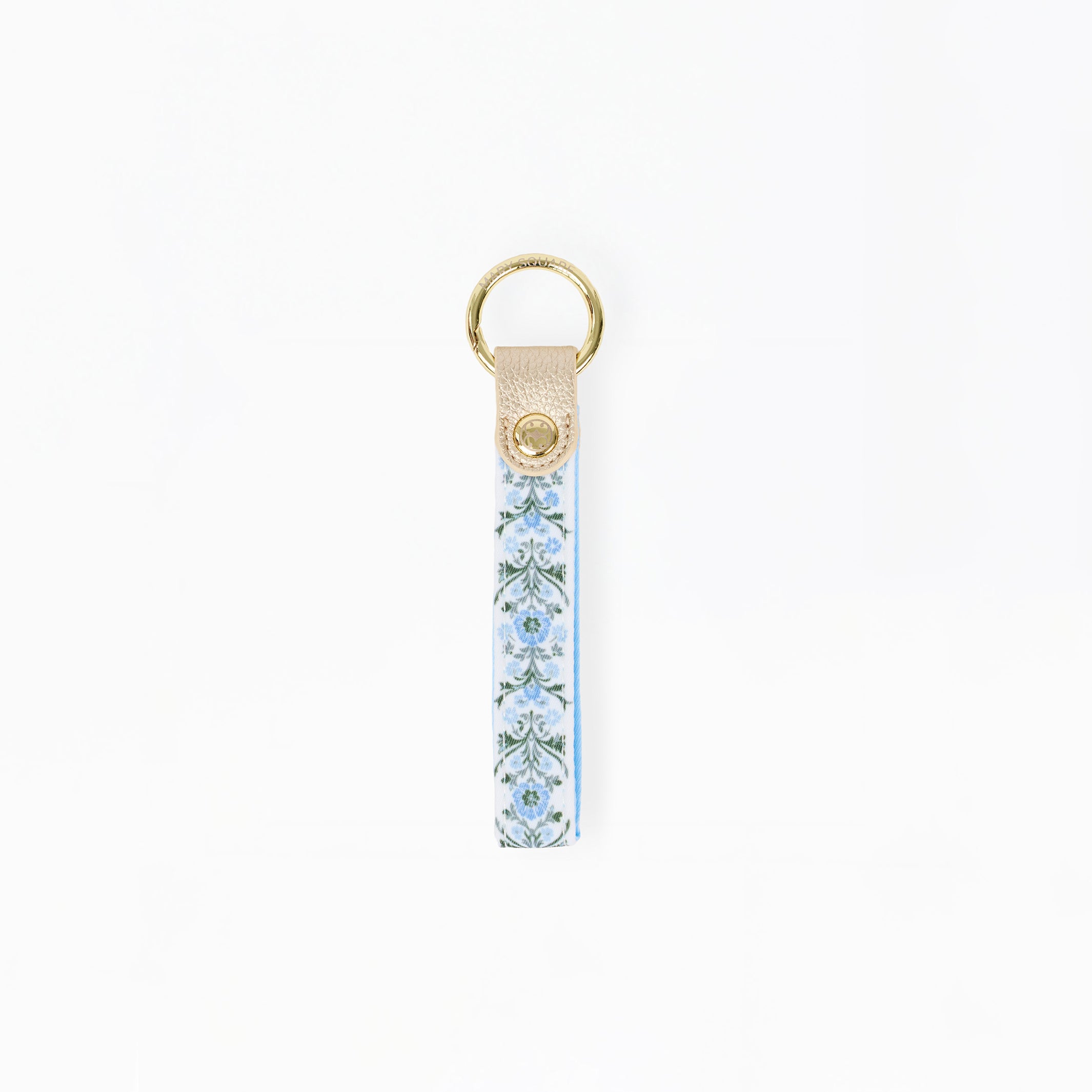 A vertical leather keychain strap featuring a light blue and white floral pattern, finished with a gold-tone metal ring and a small gold logo medallion on the leather tab.