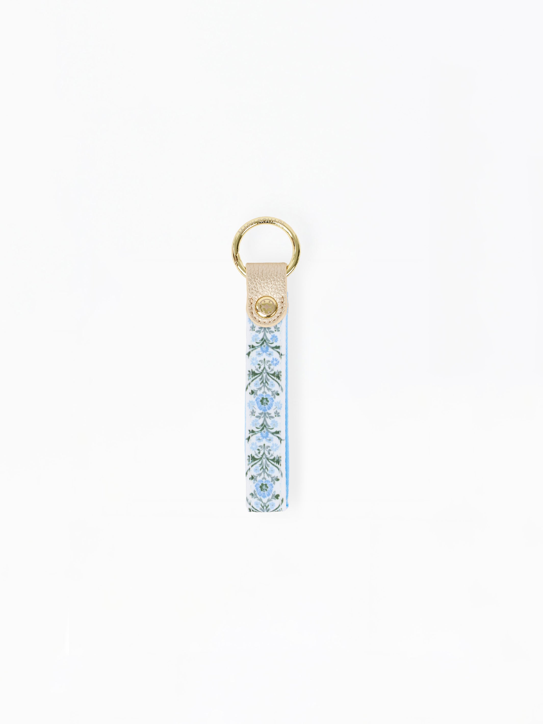 A vertical leather keychain strap featuring a light blue and white floral pattern, finished with a gold-tone metal ring and a small gold logo medallion on the leather tab.