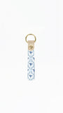 A fabric keychain strap featuring a blue and white ikat pattern, finished with a beige leather tab and a gold-tone metal key ring.