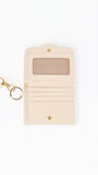 A cream-colored leather key pouch with a gold-tone keyring and clasp, featuring a clear ID window on the front.