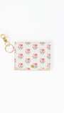 A small card holder or wallet with a white background and an all-over pink rose floral print, featuring a gold-tone swivel clasp and key ring attachment.