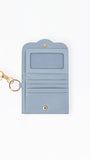 A light blue faux leather wallet with a gold-tone keychain clasp, featuring an ID window, card slots, and a snap button closure, shown on a plain white background.