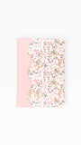 A notebook or journal cover featuring a light pink solid panel on the left and a scalloped edge with a dense pink, white, and green floral pattern on the right, shown against a plain white background.