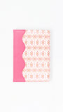 A notebook or journal with a bright pink cover on the left side and a white cover on the right featuring a delicate pink geometric pattern, separated by a scalloped pink border.