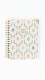 A spiral-bound prayer journal with a cream-colored cover decorated with a delicate multicolor floral and vine pattern, featuring gold foil lettering that reads 'Prayer Journal'.