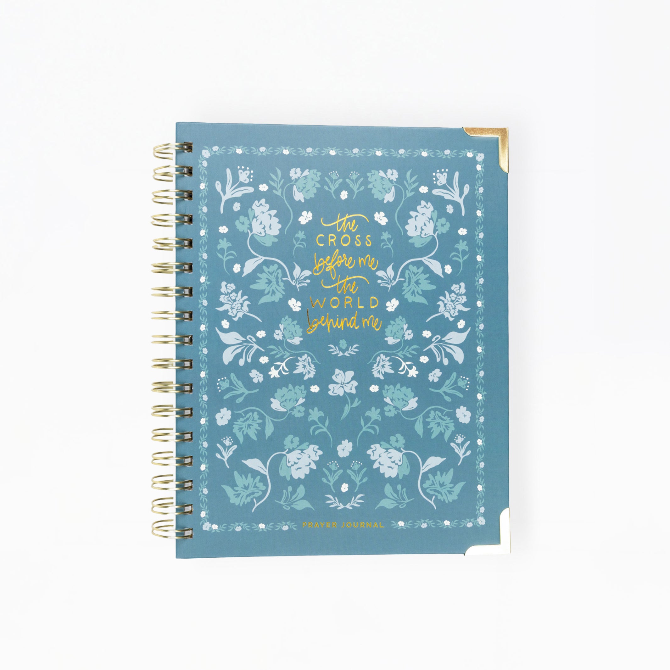 A spiral-bound notebook with a dusty blue cover decorated with white floral patterns and gold foil text reading 'with courage before me and hope behind me'.