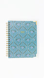 A spiral-bound planner or notebook with a dusty blue cover featuring a repeating white and purple floral pattern, shown on a plain white background.