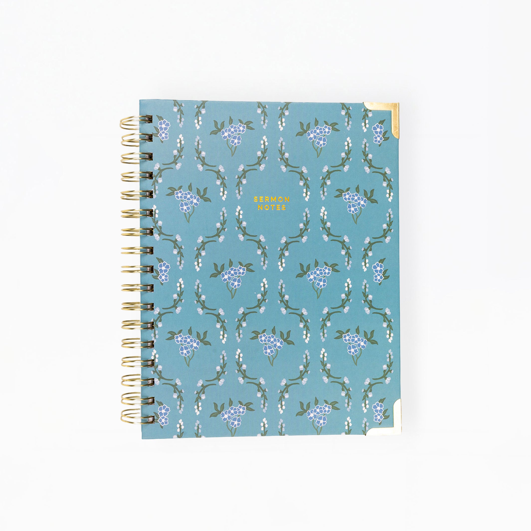A spiral-bound planner or notebook with a dusty blue cover featuring a repeating white and purple floral pattern, shown on a plain white background.
