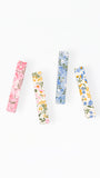 Four slim rectangular hair clips with delicate floral patterns in pink, yellow, blue, and white, arranged vertically on a plain white background.