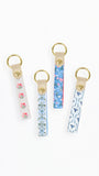 Four fabric keychains with gold-tone metal rings and snap closures, displayed on a clean white background. Each keychain has a different pattern: pink floral on white, blue floral on white, blue botanical on white, and blue abstract on white.