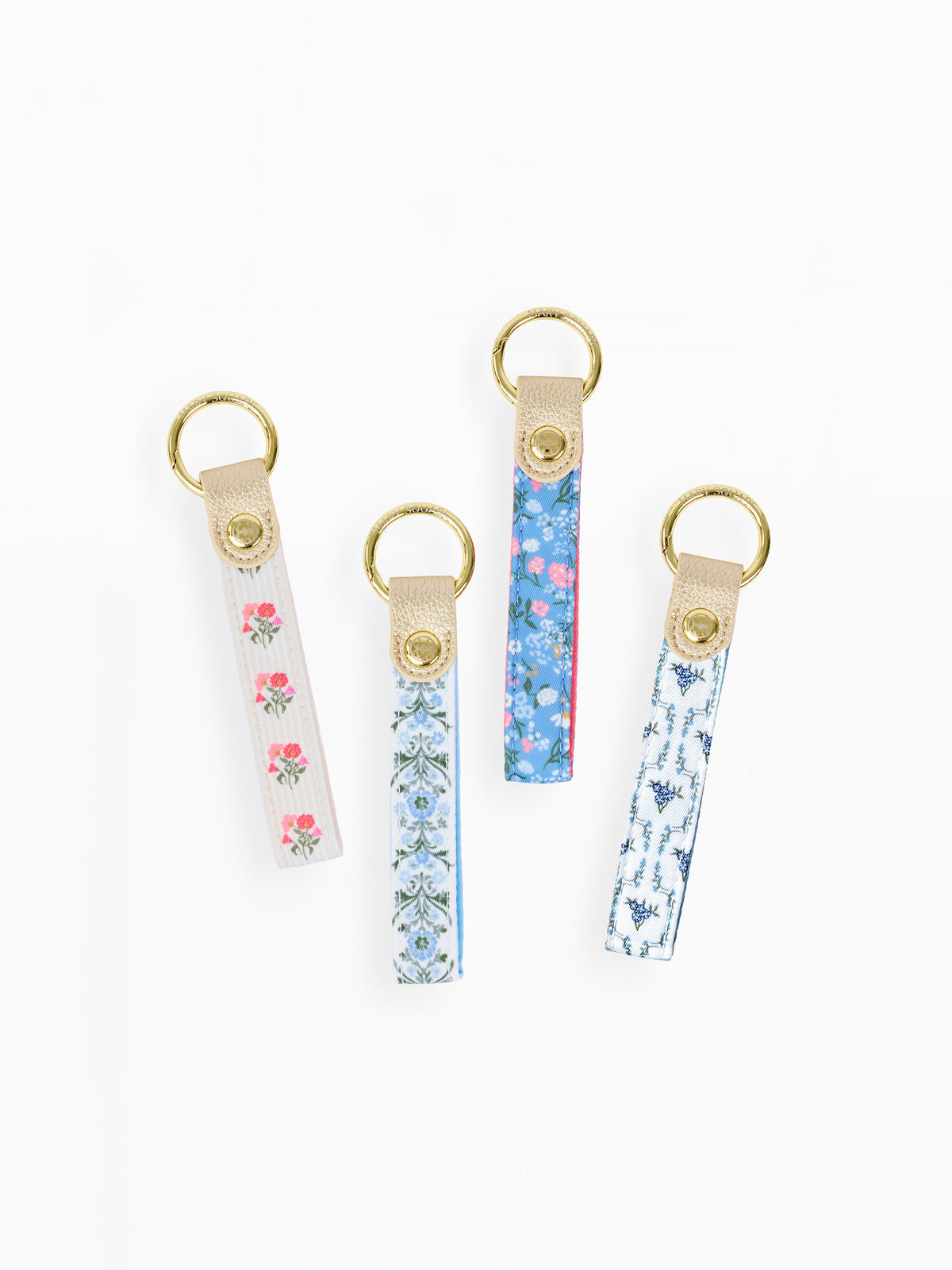 Four fabric keychains with gold-tone metal rings and snap closures, displayed on a clean white background. Each keychain has a different pattern: pink floral on white, blue floral on white, blue botanical on white, and blue abstract on white.