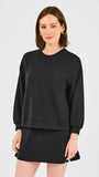 Woman wearing a black sweatshirt and skirt set on a light gray background