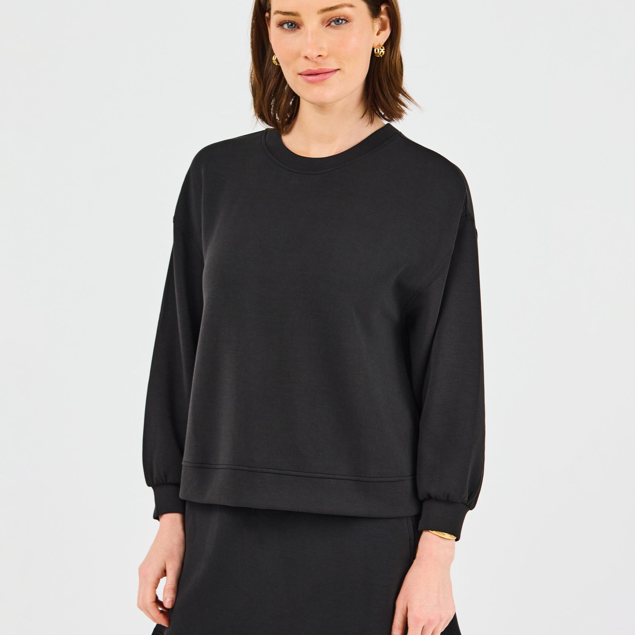 Woman wearing a black sweatshirt and skirt set on a light gray background