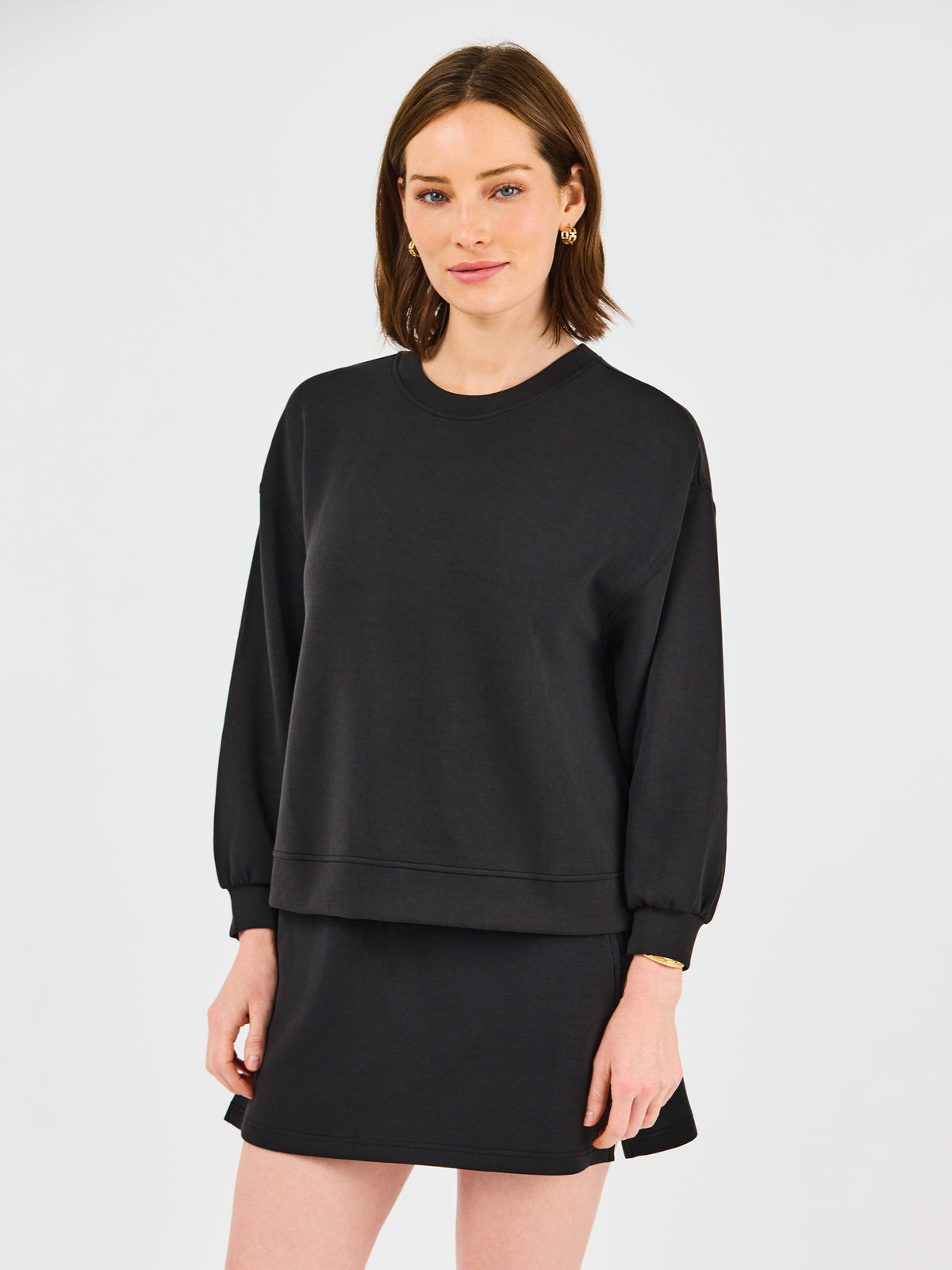 Woman wearing a black sweatshirt and skirt set on a light gray background