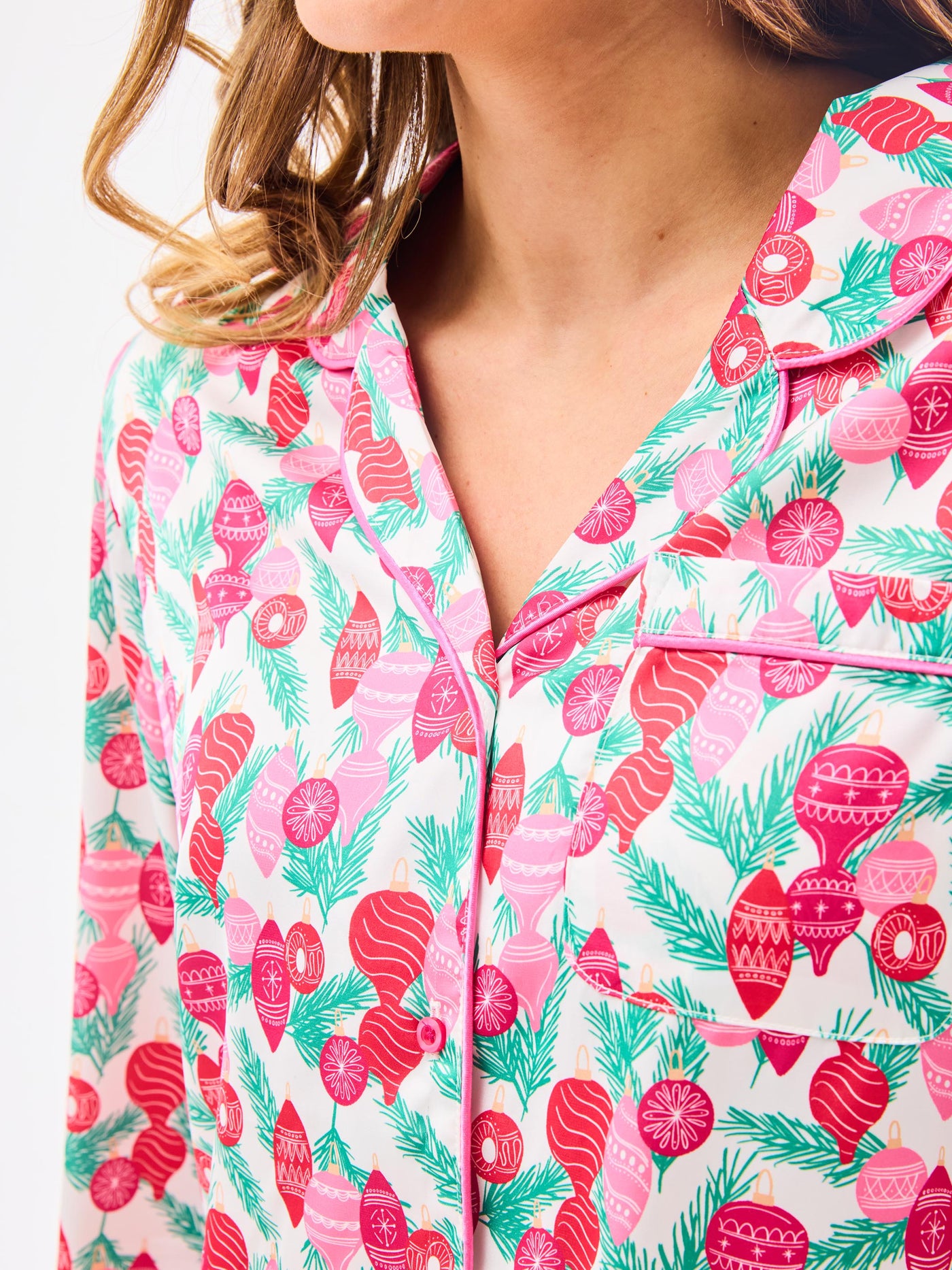 Woman wearing a christmas pajama set  with holiday ornaments in pinks, greens and reds on a white background