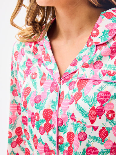 Woman wearing a christmas pajama set  with holiday ornaments in pinks, greens and reds on a white background
