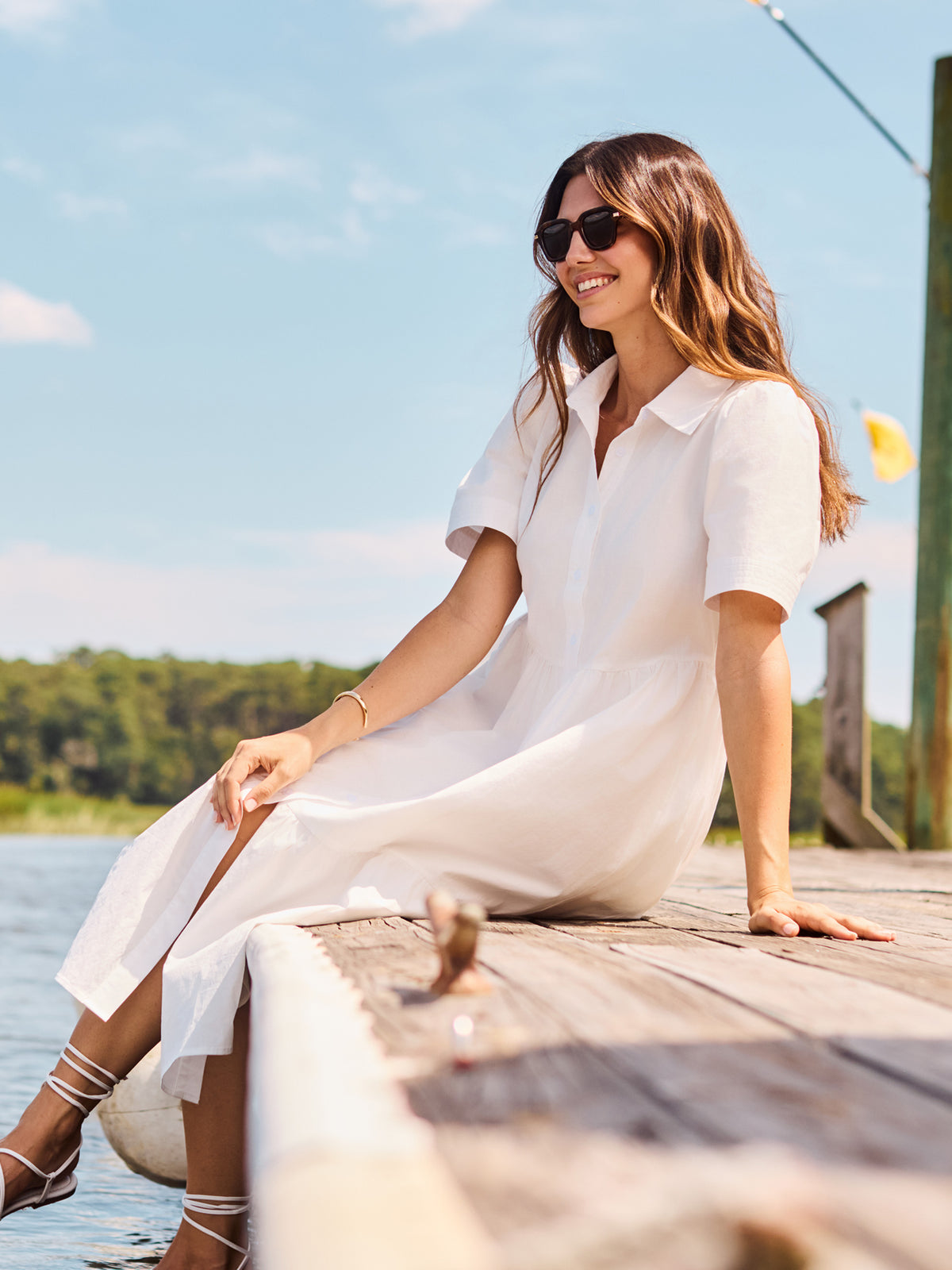 Woman in a white dress sitting on a dock by a body of water.