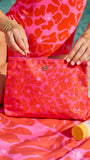 Person holding a pink floral bag with a matching swimsuit and towel on a beach.