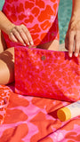 Person holding a pink pouch with a matching swimsuit and towel by a poolside.