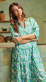 Woman in a green floral dress standing in a kitchen.
