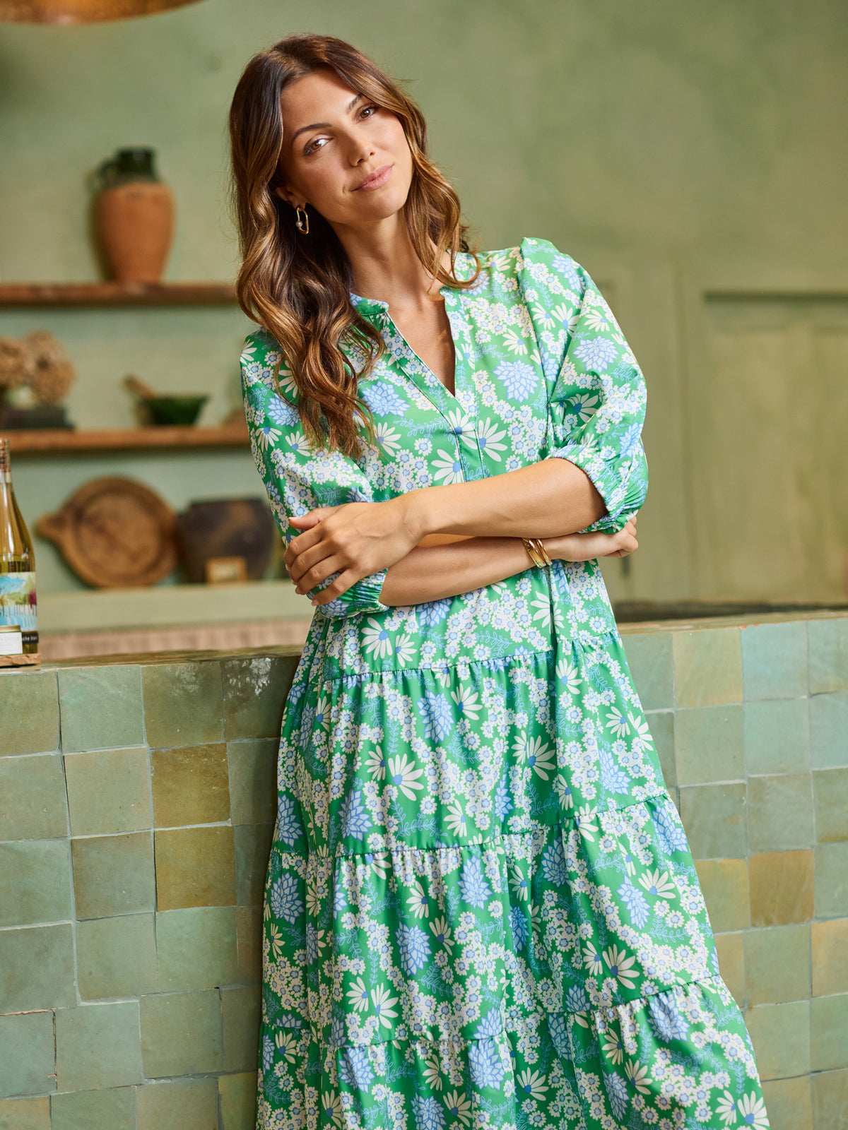 Woman in a green floral dress standing in a kitchen.