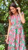 Woman wearing a pink and green floral dress standing in a garden.
