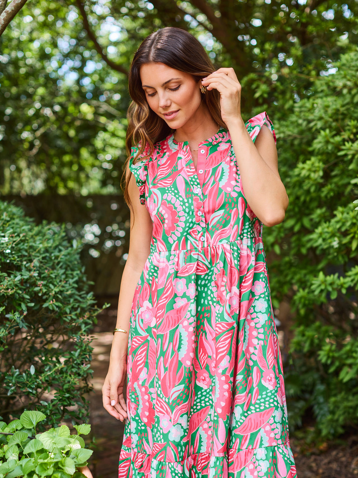 Woman wearing a pink and green floral dress standing in a garden.