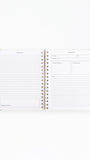 An open spiral-bound planner or notebook with lined pages and small blank boxes on the right page, photographed on a clean white background.