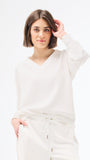 Woman wearing a white long-sleeve top against a plain background
