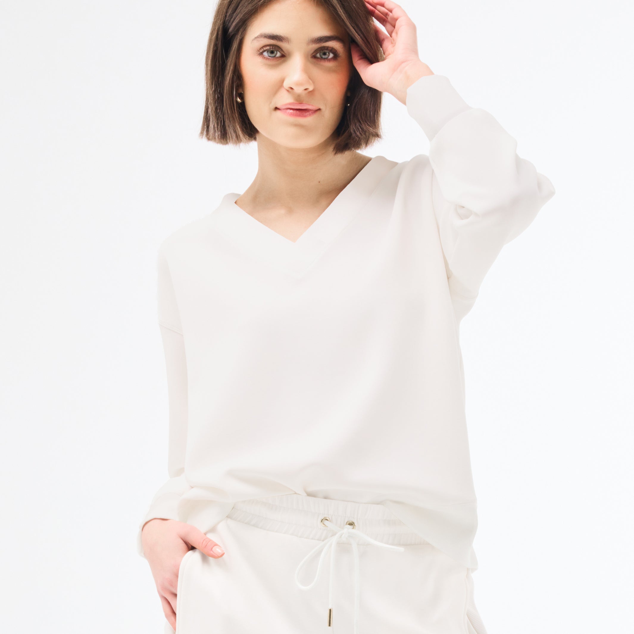 Woman wearing a white long-sleeve top against a plain background