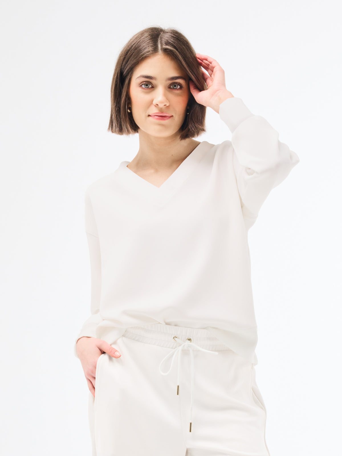 Woman wearing a white long-sleeve top against a plain background